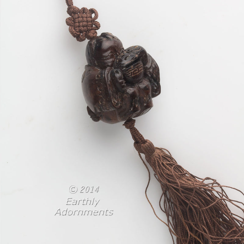 Vintage hardwood carved bead depicting a boy peering into a lidded rice bowl. with cord and tassel. China 1970's. 